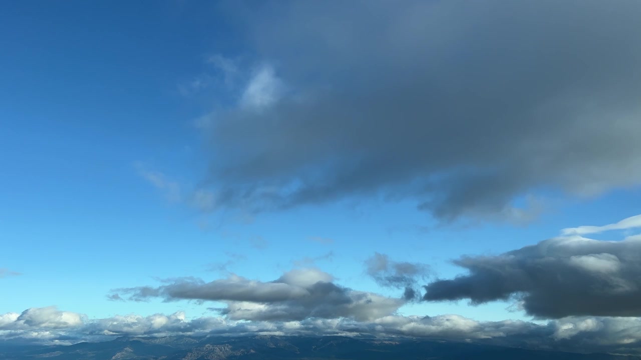 A partially cloudy blue sky shot from an airplane’s cabin before sunsen over a mountainous area North of Spain. 8000m high. A pilot’s point of view.