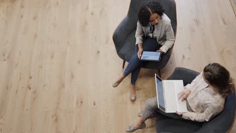 Diverse-female-colleagues-in-discussion-using-laptop-and-tablet-in-office-lounge,-slow-motion