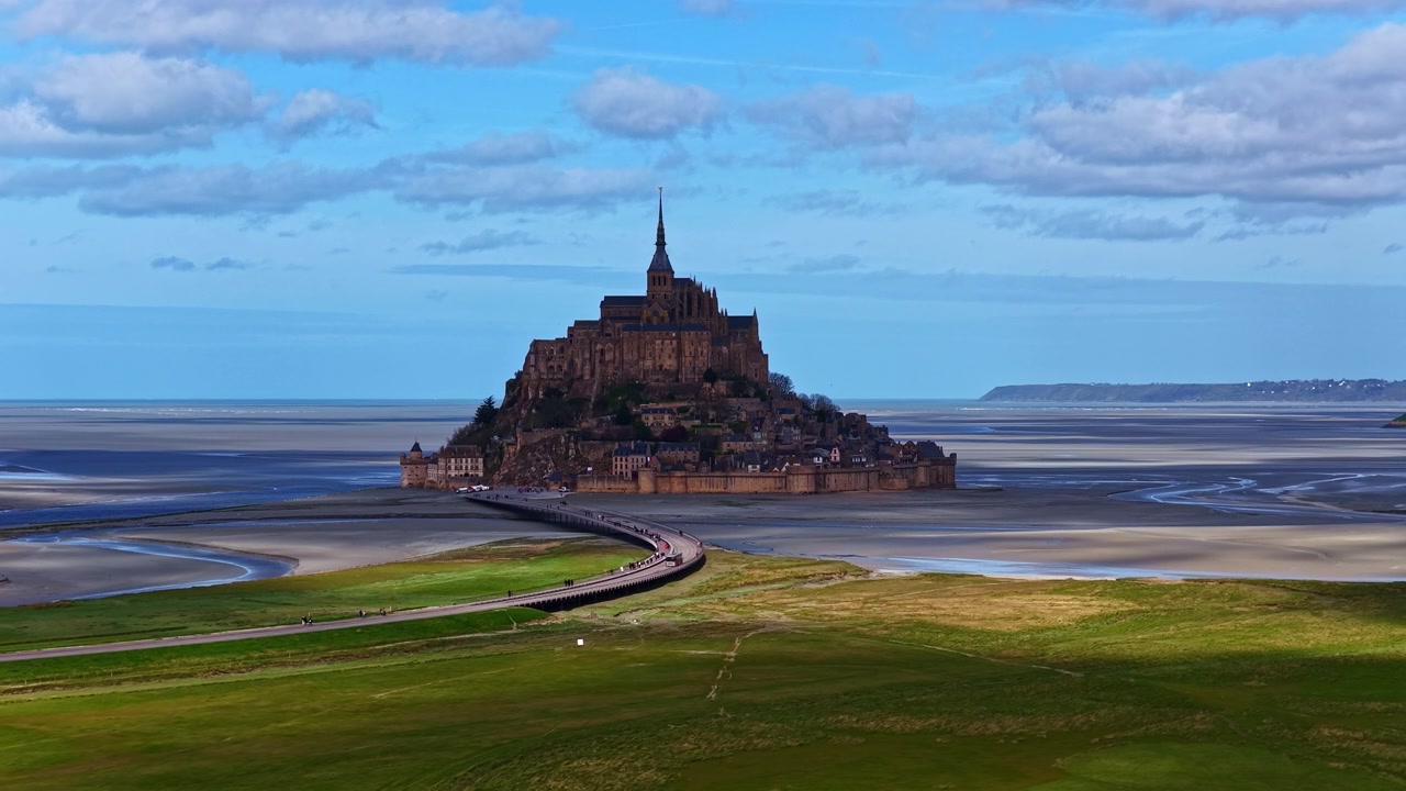 Mont Saint-Michel rejser sig prominent midt i udstrakte vadehavsområder, forbundet af en smal dæmning.