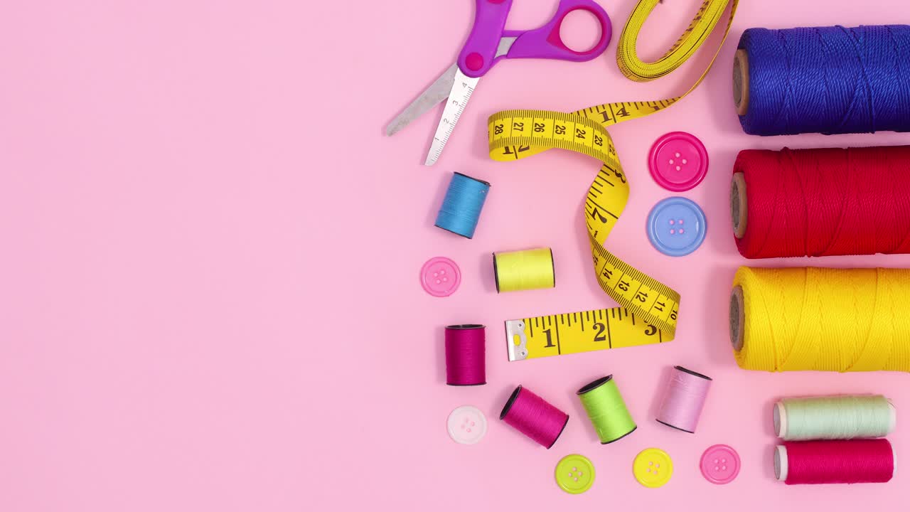 Sewing and knitting items appear on right side of pastel pink background. Stop motion flat lay