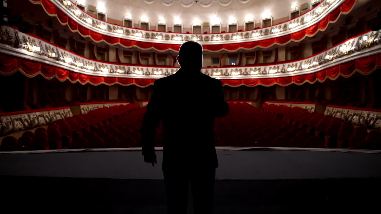 Panoramic view of a theater inside. Rear view of a presenter in the empty theater. Host on stage during the rehearsal.
