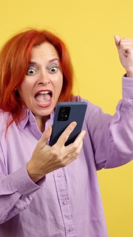 woman reacts with excitement and triumph while looking at her smartphone