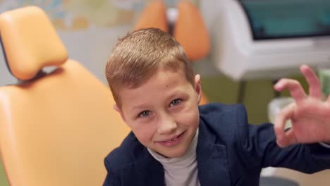 closeup portrait, little boy showing thumbs up okay in dental office