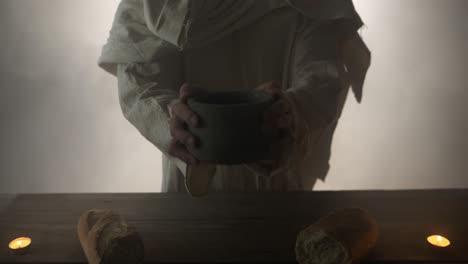 jesus christ in white robe and ambient, glowing light holding clay jar of wine as representation of the gospel, and the shed blood of jesus on the cross. easter sunday visual.