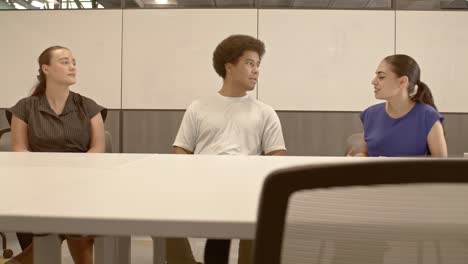 african american male, arab american female and caucasian female in their 20's in a meeting with video moving left to right with chairs in foreground