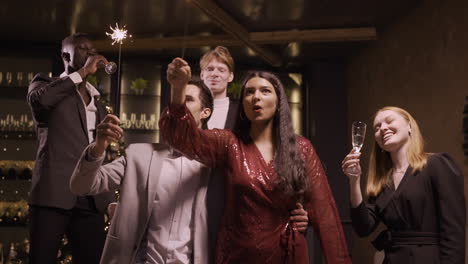 group of friends wearing stylish clothes celebrating new year eve while holding sparkles and drinking champagne