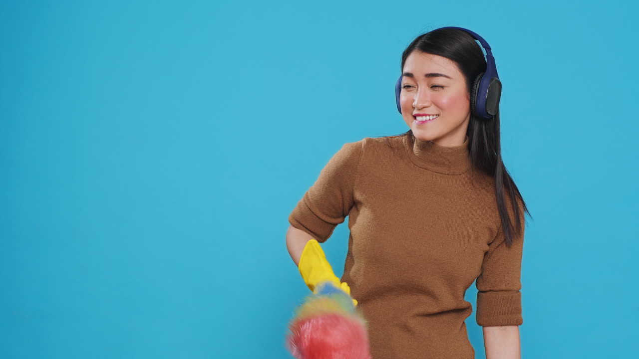 Cheeful housekeeper wearing headphones while dancing and having fun during house cleaning