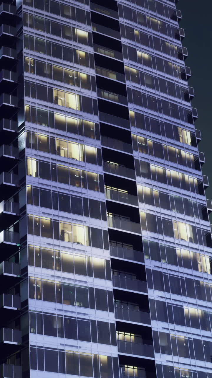 Los edificios reflejan la luz en la ciudad por la noche, con muchas ventanas oscuras.