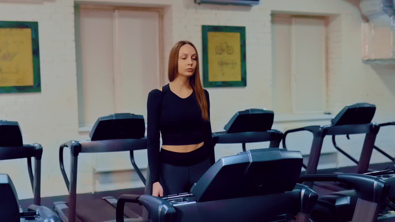 una chica hermosa va a hacer deportes en el gimnasio, calentándose. una chica camina en una cinta de correr, hace ejercicios de calentamiento. movimiento circular de la cámara.