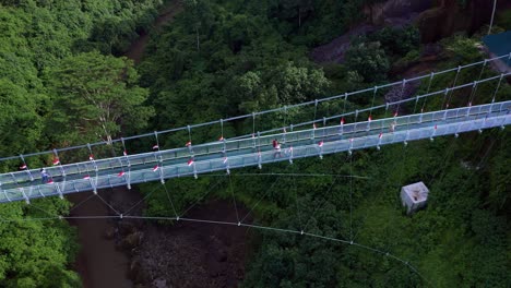 Vista-Aérea-De-La-Gente-Caminando-En-El-Puente-Con-Fondo-De-Cristal-Que-Conectaba-El-Pueblo-Tradicional-De-Blangsinga-Y-La-Cascada-De-Tegenungan-En-Bali,-Indonesia