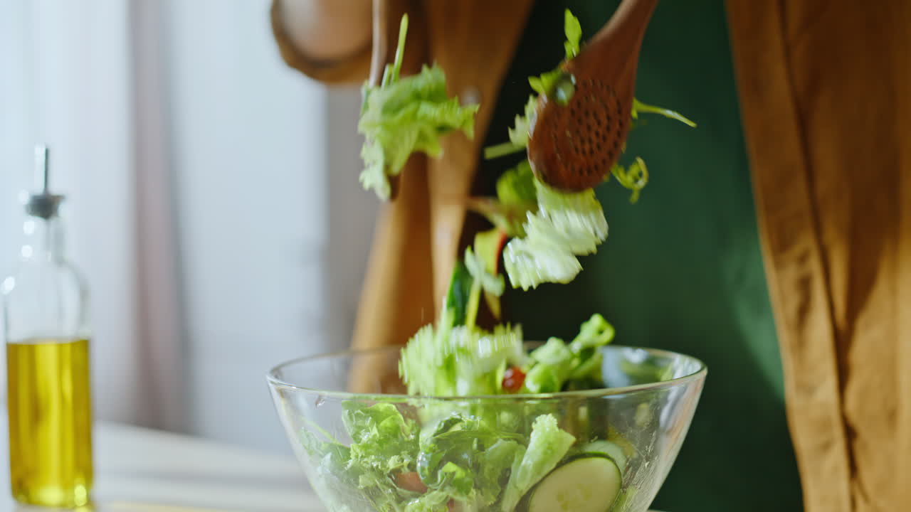 Tangan koki mencampur salad menggunakan spatula kayu di meja dapur, close-up.