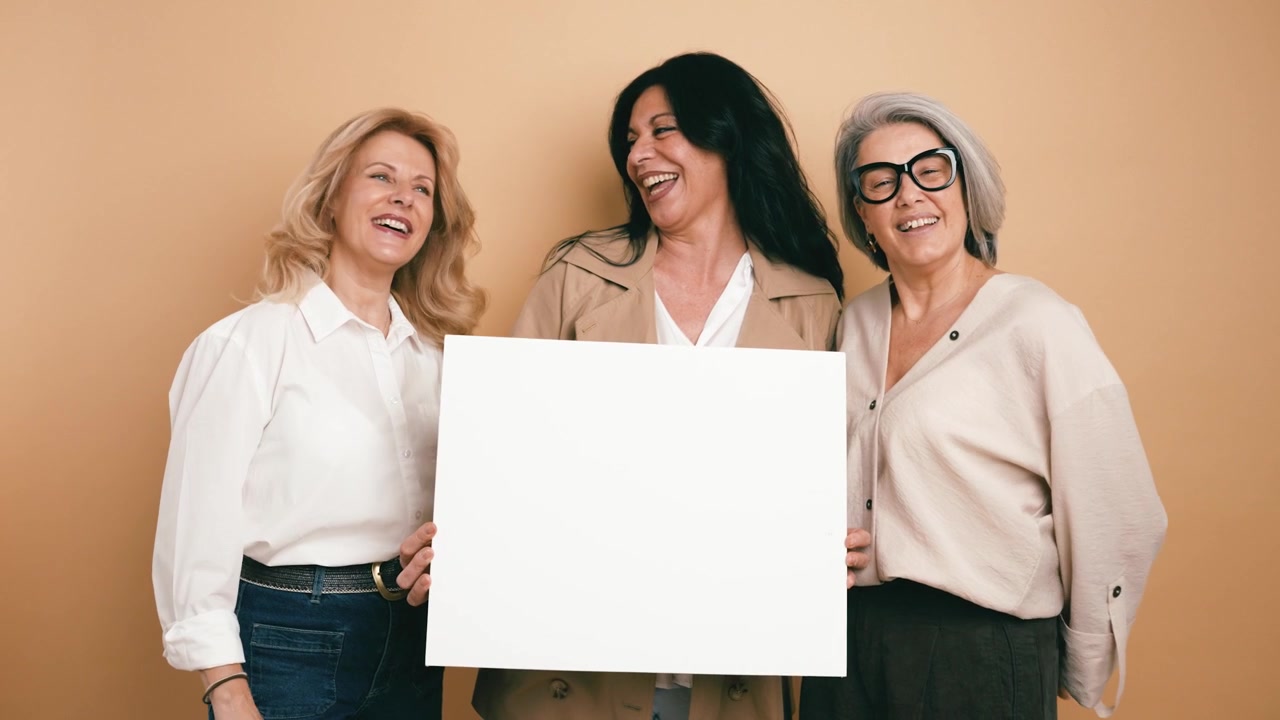 Tre donne mature che tengono un cartello vuoto su uno sfondo beige