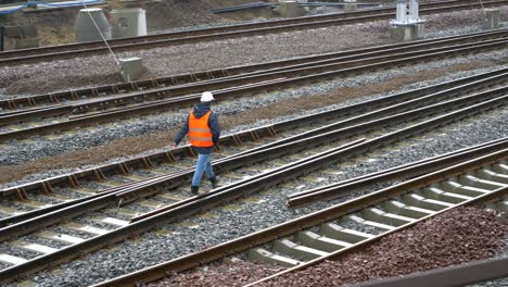 a man in work clothes is walking along the railroad tracks