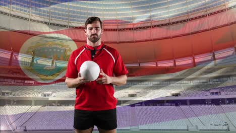 jugador de rugby profesional de pie frente a una bandera y un estadio