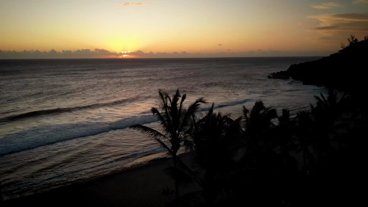 lapso de tiempo del dron parado sobre el océano mientras el sol se pone y las palmeras se mueven en el viento colores cálidos del sol
