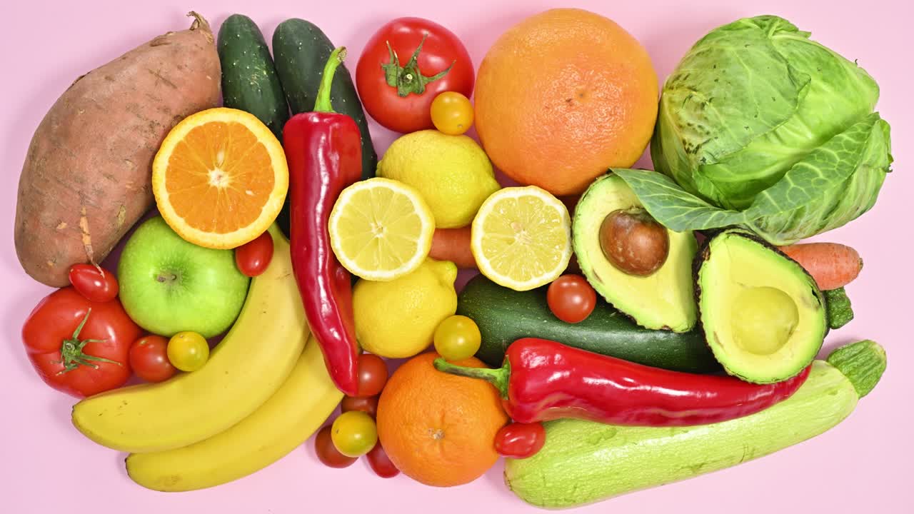 varias frutas y verduras orgánicas frescas y maduras aparecen sobre un fondo rosa pastel.