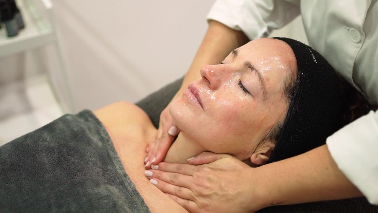 Cosmetologa che massaggia il viso di una cliente con una maschera cosmetica in un salone di bellezza.