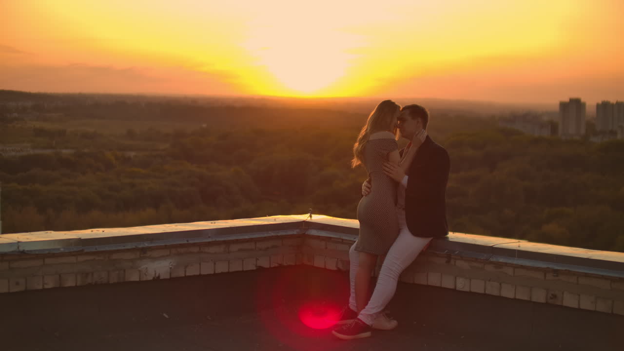 Young couple in love standing on the roof hug and closely look at each other. Romantic evening on the roof of the building. A date on the roof of a building love. Slow motion
