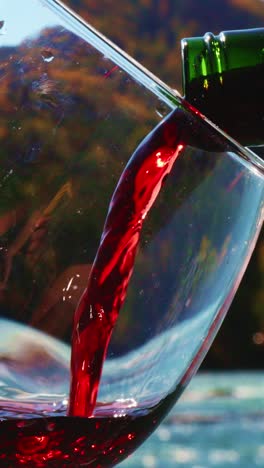 pouring red wine into a glass by a river