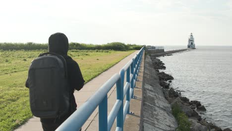 side view of man in black walking to the lighthouse from a distance