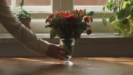 Putting-vase-with-orange-flowers-on-wooden-table-by-female-hands