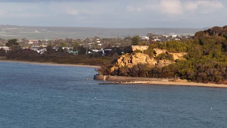 daytime camera pan reveals rocky headland, calm bay, distant houses, and soft natural lighting