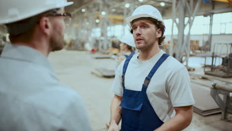 factory worker giving handshake and talking to engineer in industrial warehouse