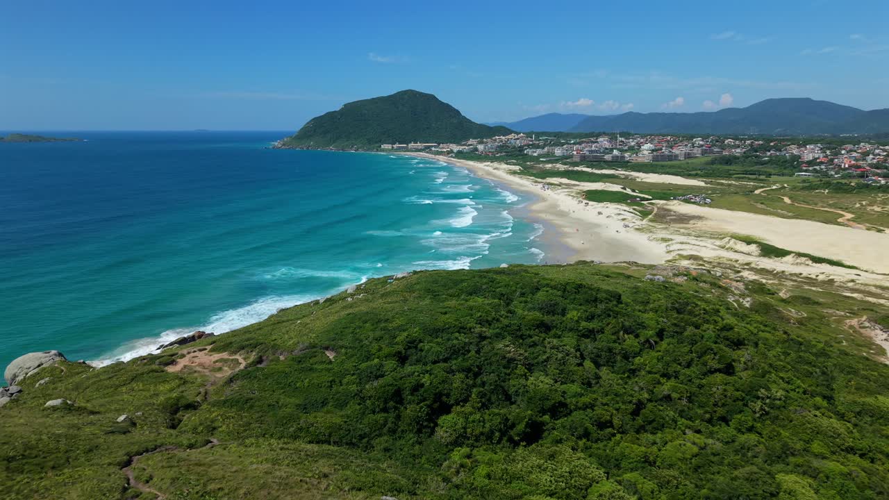 Spiaggia costiera con acqua turchese e dune lungo Praia do Santinho a Florianopolis, Santa Catarina, Brasile