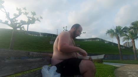 Hombre-Obeso-En-Topless-Expone-Su-Barriga-Gorda-Y-Cervecera-Mientras-Come-Un-Puñado-De-Papas-Fritas-En-Un-Banco-Del-Parque