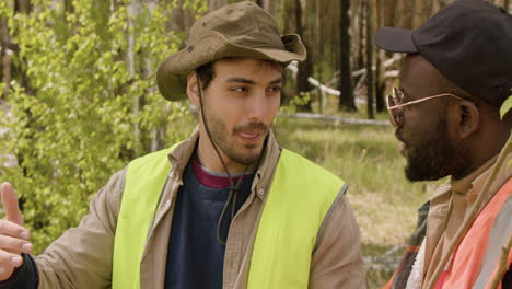 close-up view of caucasian and african american men activists watching something in a tablet and deciding where to plant the trees