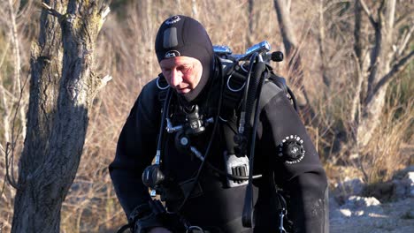 a diver dressed in black with his oxygen cylinders descends from the forest to the lake