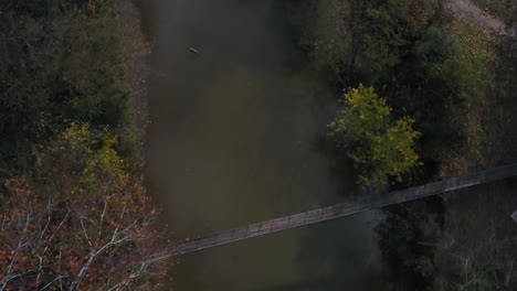 Drone-shot-of-a-suspension-bridge-over-a-river-in-the-woods-during-the-autumn-season