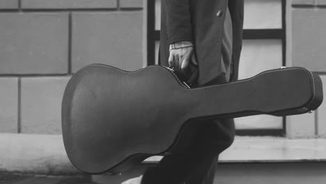 black and white and side view of man carriying a guitar case walking in the street