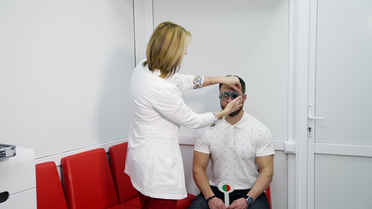 Eyesight test in clinic. Female optician in lab coat adjusting lens in trial frame of a patient. Doctor covers another eye with a lens in testing glasses. Slow motion.