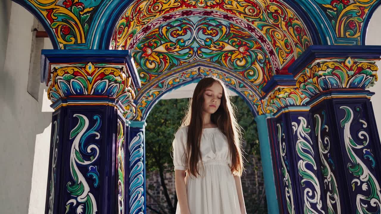 Young girl wearing white dress standing beneath ornate Romanian style archway, vibrant colors framing delicate feminine silhouette against traditional architectural background