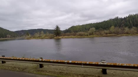 Driving-next-to-a-river-in-Oregon-with-beautiful-Douglas-Fir-tree-covered-mountains-in-the-background