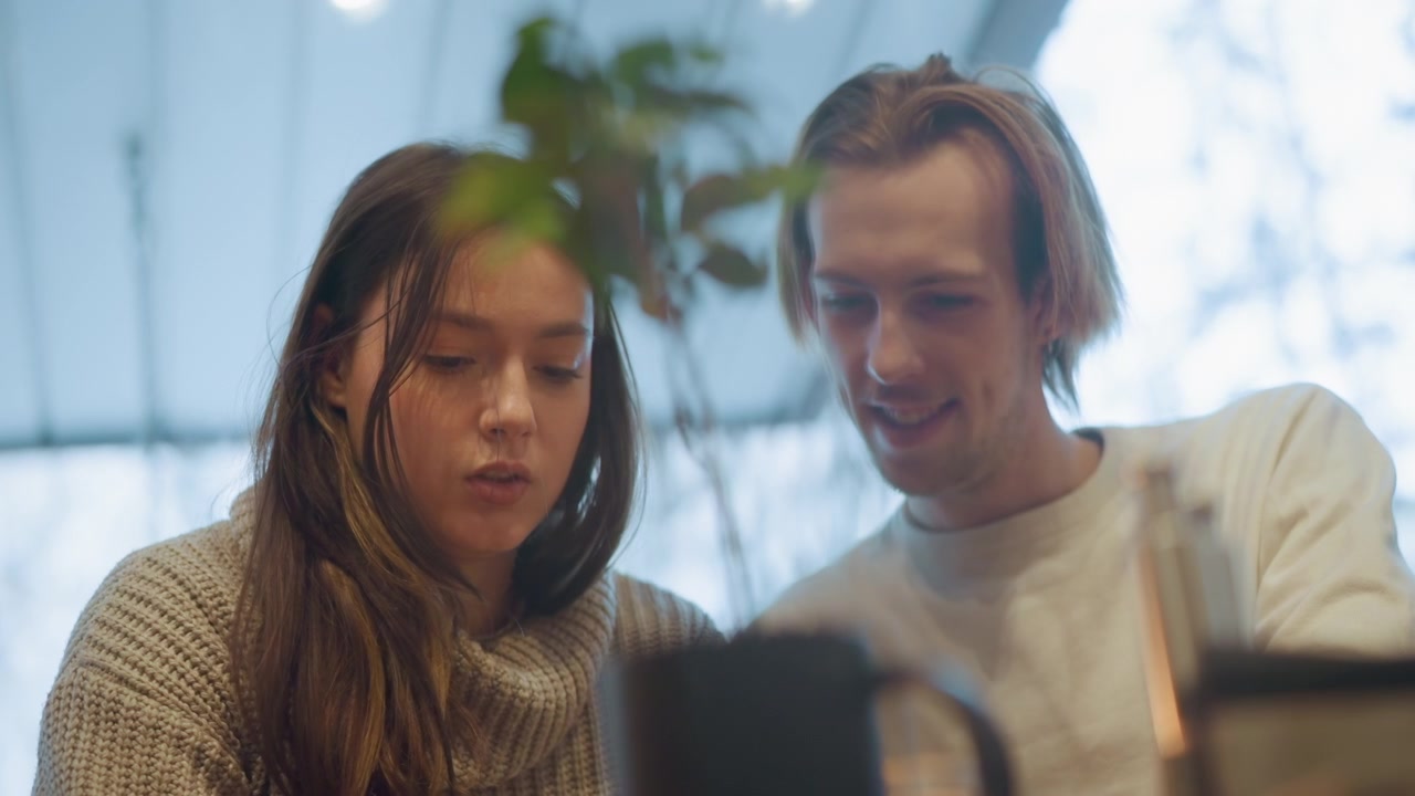 Close up of two people woman and man looking at object together in soft lighting. scene includes fine details like texture of their clothing and nearby objects such as cups on table