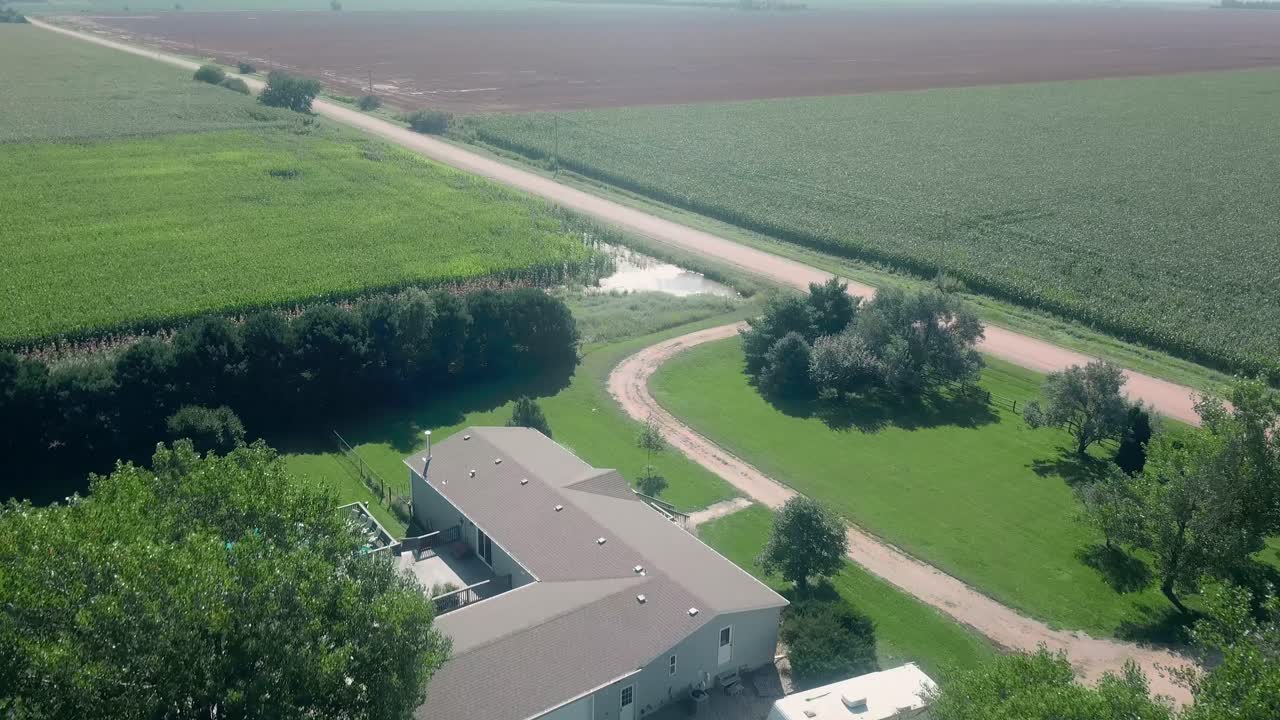 vista aérea de drones de una casa en expansión, un patio de granja, agua estancada, campos de maíz y un camino de grava en la zona rural de nebraska, ee.uu.