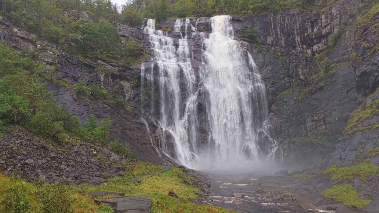 Drönarvy en stämningsfull dag över vattenfallet Skjervefossen och en man nära en klippa i Norge