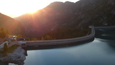 aerial drone shot of water dam and lake fedaia in dolomites in italy just before sunset behind the mountain in background