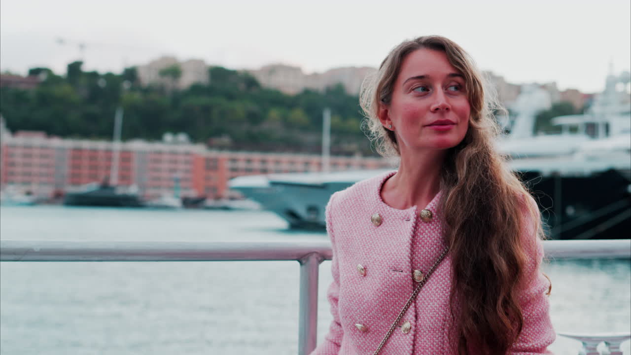 Brunette kvinde i en pink blazer foran både, der ligger til kaj i Monaco Marina