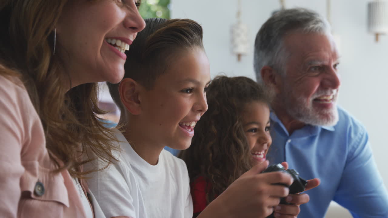 Hispanic Grandparents With Grandchildren Playing Video Game At Home Sitting On Sofa Together