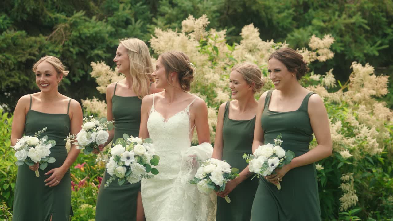 Sposa e damigelle camminano in un giardino ridendo insieme al rallentatore
