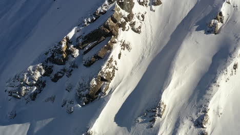 Aerial-view,-rising-up-above-a-snow-covered-mountain-peak-in-the-French-Alps