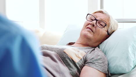 Close-up-of-old-sick-woman-lying-in-bed-talking-with-a-male-assistant