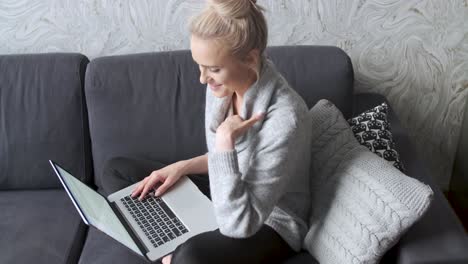 Middle-aged-woman-sitting-on-sofa-in-her-living-room-and-working-on-laptop