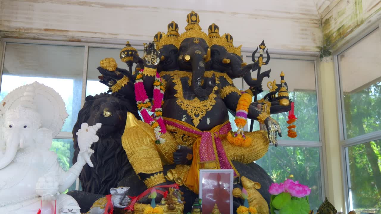 Close-up de uma estátua preta de Ganesha (Phra Phikanet) com várias cabeças e braços, sentada em um leão. Adornada com flores e faixas no templo Wat Nai Harn em Phuket, Tailândia. Filmagem de viagem em vídeos em 4K