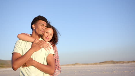 biracial couple embraces warmly on a sunlit beach, eyes closed in contentment, with copy space