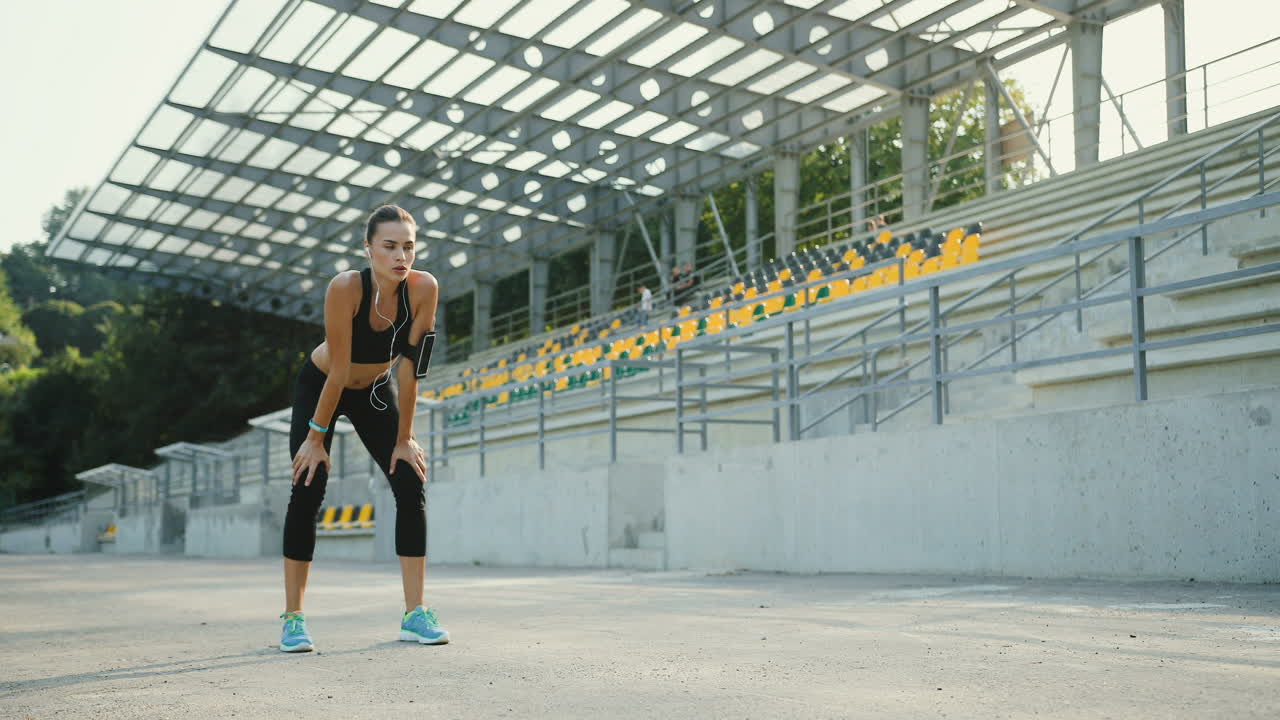 joven corredora entrenando en el estadio, luego se detiene y sigue trotando en una mañana soleada de verano