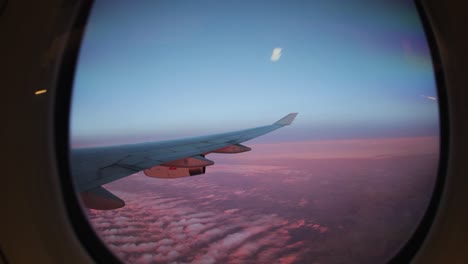 view from airplane window above light pink coloured clouds